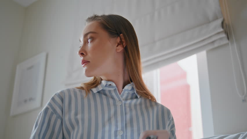 Worried girl waiting sms looking smartphone screen in white bedroom interior closeup. Serious woman messaging by mobile phone sitting apartment bed. Sad lady typing message on cellphone at morning.