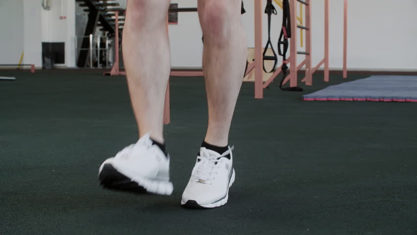 Low section of male legs skipping with jump rope. Male athlete wearing white shoes exercising at gym. He is doing crossfit training in GYM.