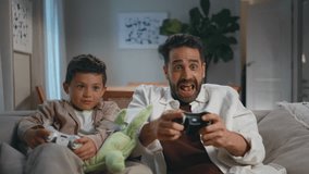 Excited gamers family playing video game at dark home closeup. Cheerful father small son holding controllers enjoying videogame at living room. Emotional man boy using joysticks together at house - Powered by Shutterstock - Get 15% off with code: PIKWIZARD15