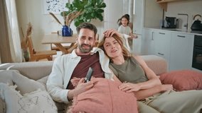 Happy family embracing sofa at home closeup. Attractive mother father watching tv at cozy room. Funny kids hugging parents jumping at couch. Smiling people enjoying time together. Happiness concept  - Powered by Shutterstock - Get 15% off with code: PIKWIZARD15