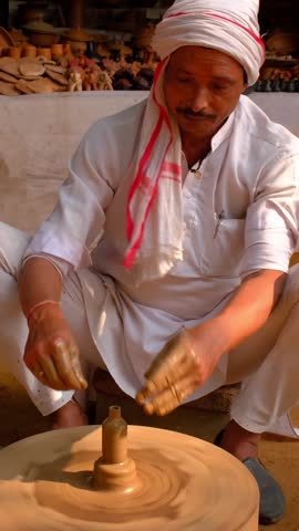 Skilled professional potter throwing the potter's wheel and shaping traditional ceramic vessel and clay ware: pot, jar in pottery workshop. Handwork craft from Shilpagram, Udaipur, Rajasthan, India