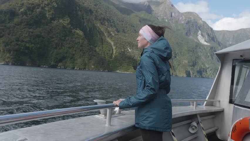 Young caucasian woman in a jacket riding a boat through a fiord on a sunny summer day in Milford Sound, Fiordland, New Zealand.