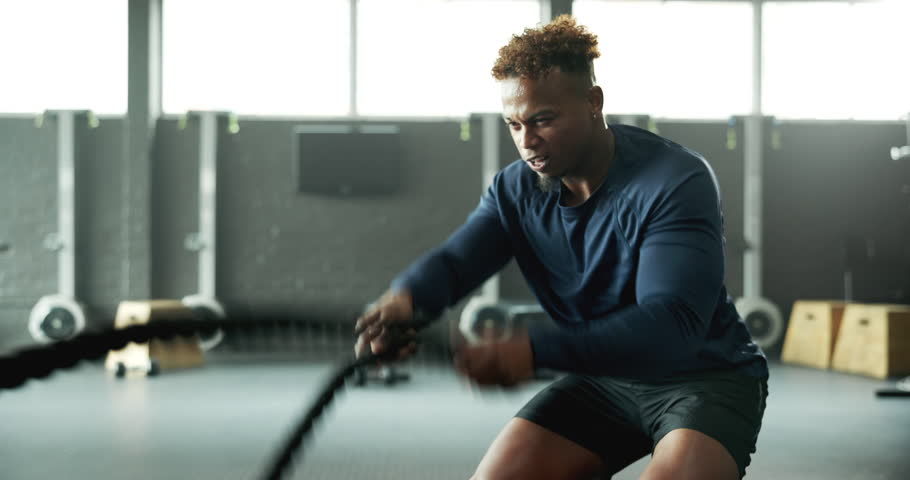 Man, battle rope and fitness in gym, cardio exercise and muscle building for workout. Intense routine, moving and body wellness with power or strength training, weight equipment and bicep challenge