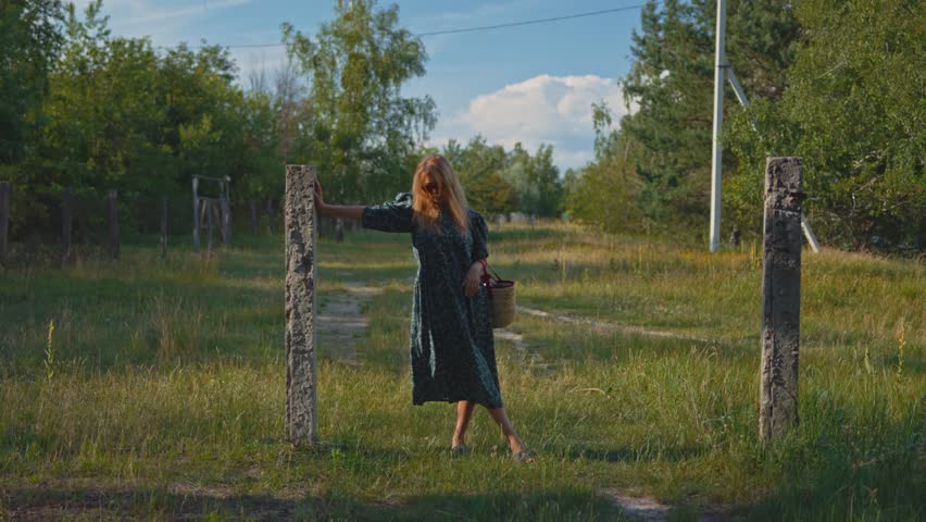 Portrait of a young stylish woman in a turquoise dress and a straw hat with a straw bag in the village