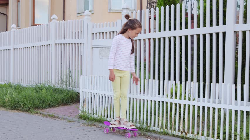 Joyful little girl child with hair bun skating down the road enjoying the healthy lifestyle and the thrill of being a little skateboarder on city street