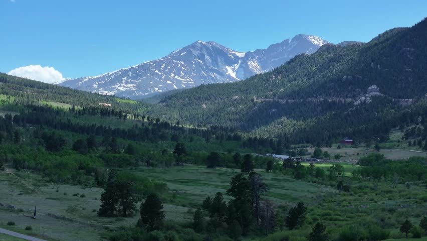 Flying over forests and and a valley toward snow capped peaks in Estes Park Colorado