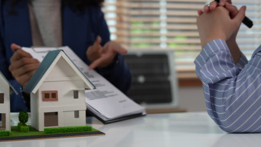 Real estate broker agent presenting and consult to customer to decision making sign insurance form agreement, home model, concerning mortgage loan offer in office.