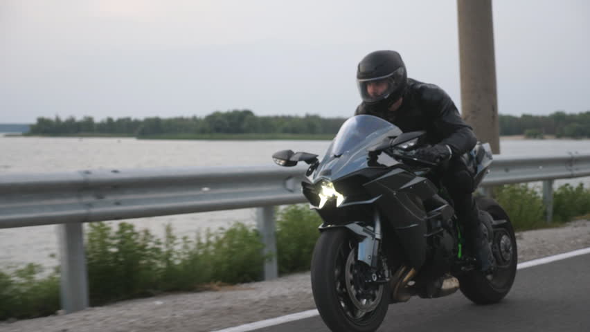 Close up of biker driving motorbike during road trip near river or lake. Man ride fast on modern sport motorcycle at country road. Motorcyclist racing his bike on rural route. Concept of adventure