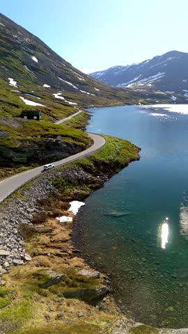 A winding road alongside a beautiful, clear lake surrounded by mountains. Snow still covers the peaks. Langvatnet, Geiranger, Norway