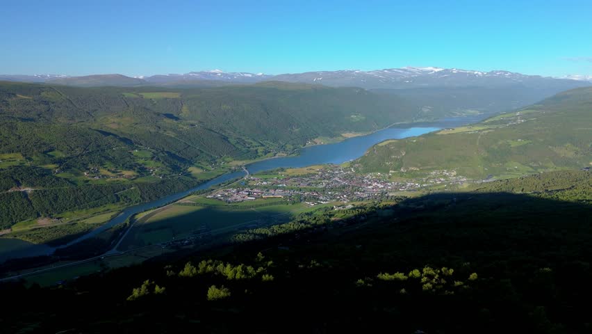 Aerial view of picturesque valley with town by the lake, surrounded by lush green hills and distant mountains. Vagavatnet Lalm Norway