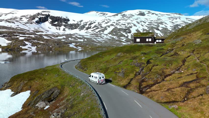 A breathtaking journey along a mountain road by a tranquil lake, surrounded by snowy peaks and lush greenery. Langvatnet, Geiranger, Norway