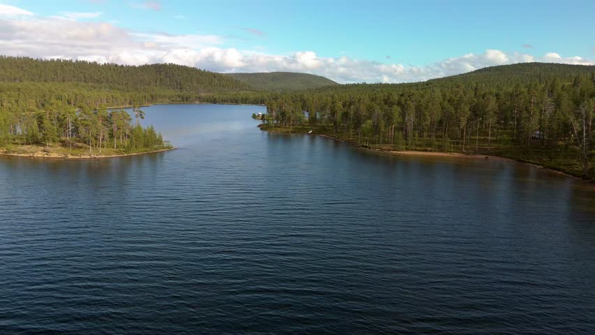 In perfect weather conditions, a serene lake is beautifully framed by dense forest under a clear sky, in Finland Lapland