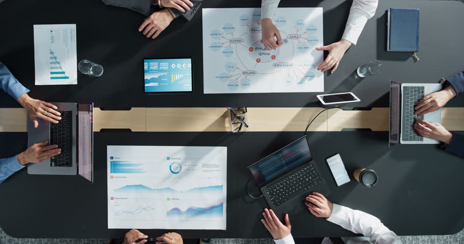 Top Down View, Zoom Out: Diverse Professionals Working on Business Statistics Reports and Digital Plans in an Office. Discussion and Data Analysis on Laptops and Charts. Teamwork, Innovation Concept.
