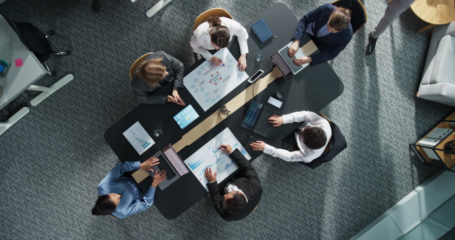 Diverse Professionals Working on Business Statistics and Marketing Plans in Corporate Office. Top Down View Of Discussion and Financial Data Analysis on Laptops and Charts. Teamwork And Innovation.