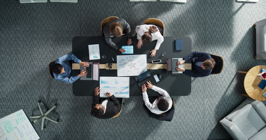 Top Down View: Diverse Team of Professional Managers And Specialists Analyzing Business Data and Strategies in Corporate Office. Collaboration Of Colleagues With Laptop Computers, Mindmap, And Graphs.