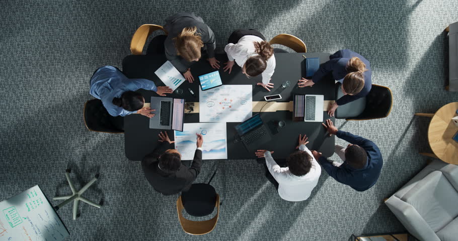 Zoom Out Top Down View: Diverse Team Of Business Professionals With Laptops Entering The Conference Room And Sitting Behind Table To Discuss Financial Data And Project Mindmap in Corporate Office.