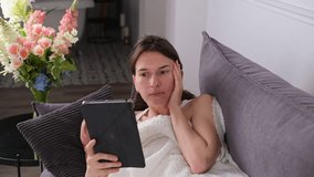 a woman lying on the couch with a tablet and making a video call with friends or family