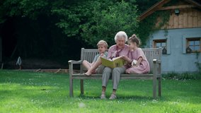 Video of two siblings with grandmother, sitting on bench in the garden, reading book together. Grandson and granddaughter enjoying together time with elderly grandma, looking at photos from photo - Powered by Shutterstock - Get 15% off with code: PIKWIZARD15