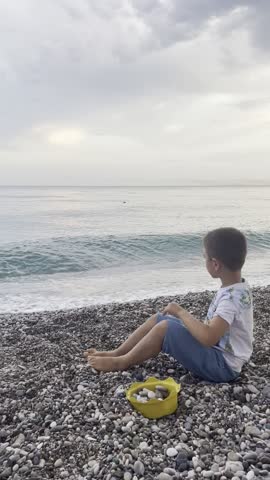 a child sits on the seashore and throws stones into the water