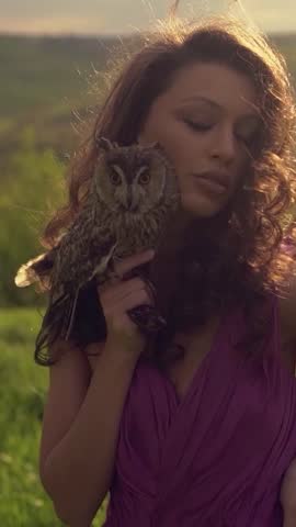 Beautiful woman with owl in purple dress in nature