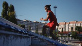 Slow motion. Profile of a young athlete man in sunglasses and dreadlocks, who is warming up by jumping on the steps of a city stadium. A man trains using jumps while outdoors on a warm autumn day on - Powered by Shutterstock - Get 15% off with code: PIKWIZARD15