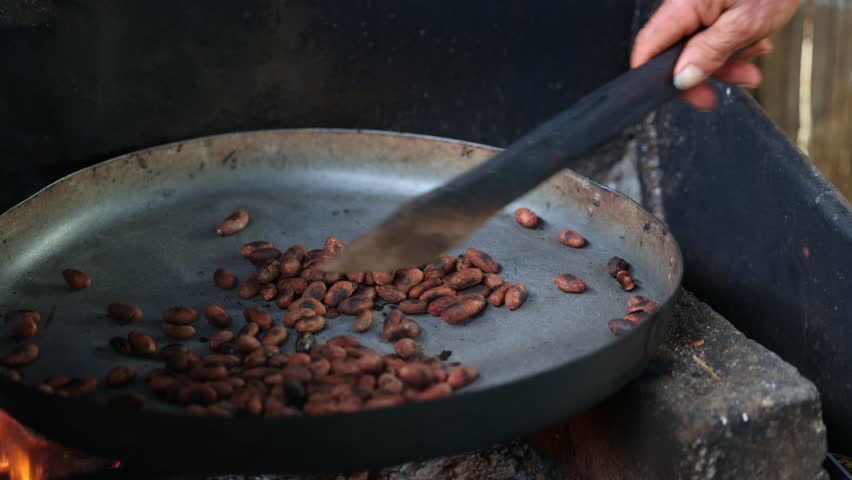 close-up of an indigenous man skillfully roasting cacao beans over an open fire using a machete, as part of the artisanal chocolate-making process.