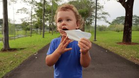 Toddler boy eagerly removes his medical mask with both hands, delighted to be mask-free in the park. His face lights up with newfound liberty as he enjoys fresh air. - Powered by Shutterstock - Get 15% off with code: PIKWIZARD15