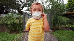 Toddler boy with wide, cautious eyes slowly removes his mask in a green park. Initially hesitant, he becomes happy and liberated, smiling with the joy of breathing freely. Renewed freedom concept - Powered by Shutterstock - Get 15% off with code: PIKWIZARD15