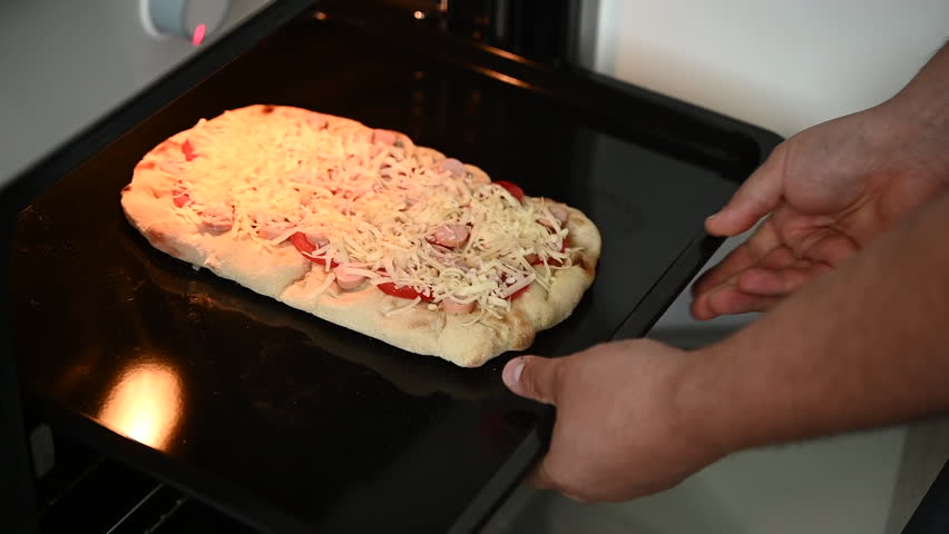 man putting pizza in oven, preparing dinner at home