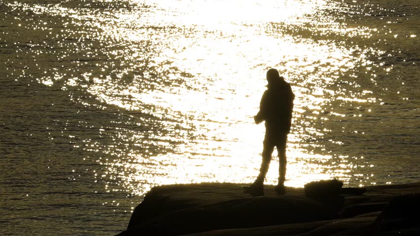 Person fishing from a cliff at sunset