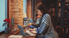 Two students collaborate at window-side desks in library, focusing on laptop and notebook. Another student walks by with book in cozy atmosphere. Concept of teamwork and productive study sessions - Powered by Shutterstock - Get 15% off with code: PIKWIZARD15