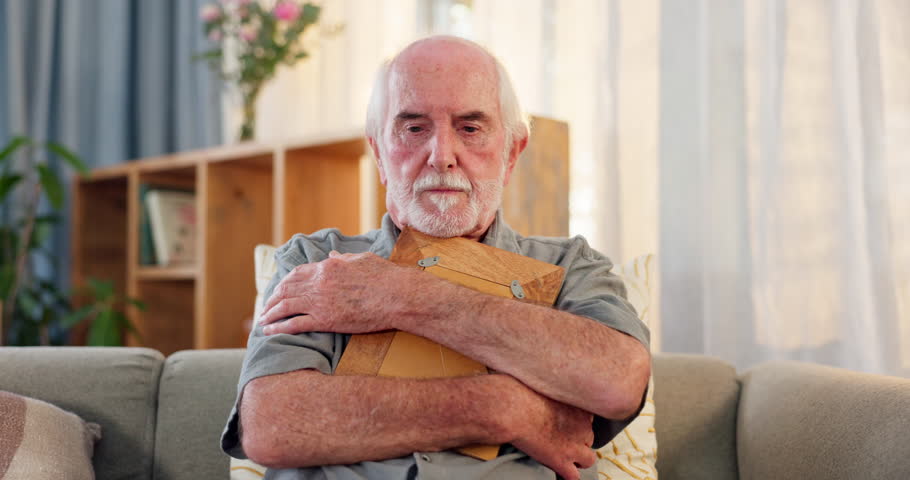 Senior, man and thinking with photograph on couch for reminiscing, nostalgia and remember memory of history or past. Elderly person, hug and sad on sofa with picture, missing and mourning in home.