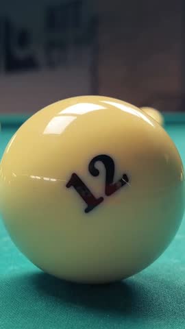 Vertical video. Shiny smooth white ivory billiard ball with number 12 on green pool and snooker table. Camera rotation. Hobby, sport bar, betting, excitement, relax, holiday. Luxury leisure in club