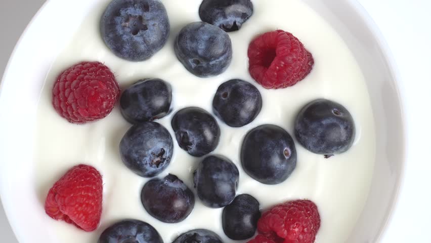 Greek yogurt with raspberry and blueberry scooped with spoon from a Bowl, close up, top view