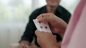Close-up of hands holding playing cards, showing 5 of clubs and 8, 6 of hearts. Blurred background of person in dark shirt. Senior friends enjoying card game in bright indoor setting. - Powered by Shutterstock - Get 15% off with code: PIKWIZARD15