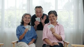 Handheld video of Senior Asian friends playing cards together and showing cards while waving greetings, friendship in bright living room - Powered by Shutterstock - Get 15% off with code: PIKWIZARD15