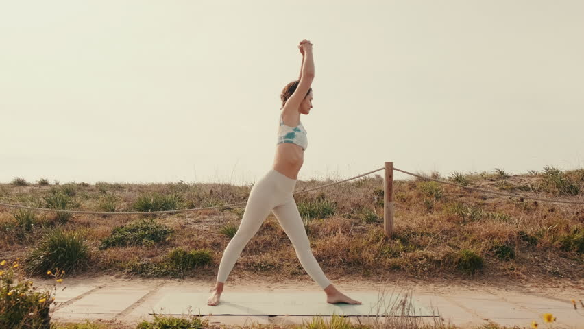 Healthy sports lifestyle. Athletic young woman in sport clothes doing fitness exercise standing in an intense side stretch pose or Pyramid, Parsvottanasana. Fit woman in nature in the summer