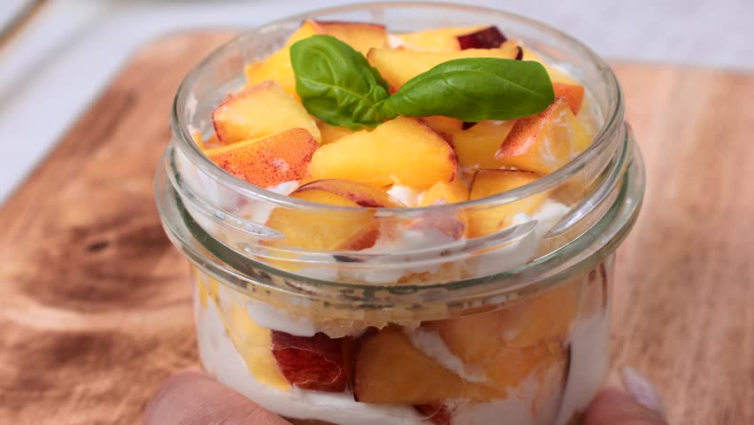 Homemade peach shortcake trifle cup with fresh peaches and whipped cream taking with a fork for eating close up