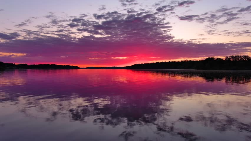 Speed boat blasts through tranquil waters reflecting red dawn sky at sunrise.
