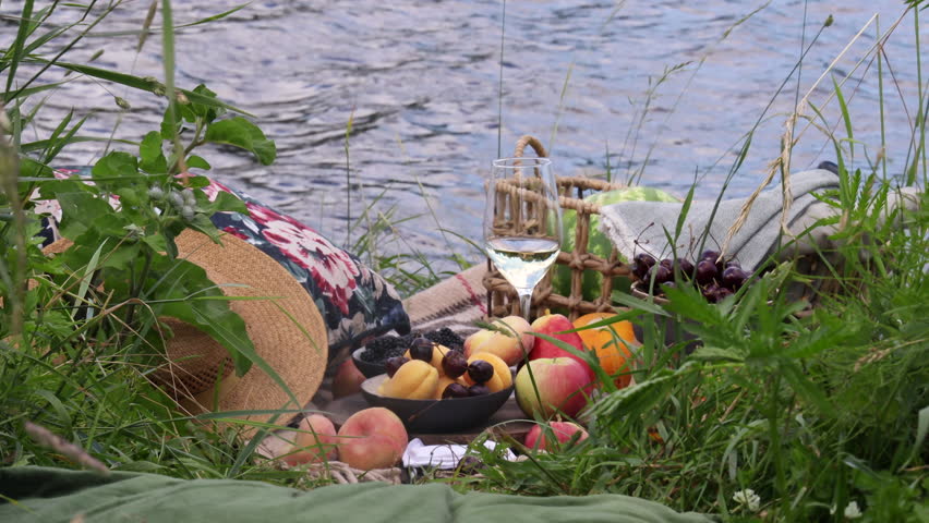 picnic in nature with fruit and wine on the river bank on a summer day 