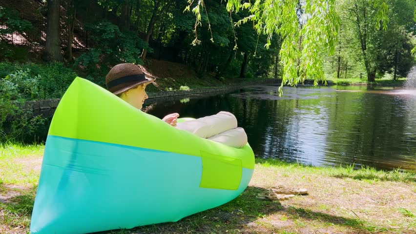 A young girl rests in a hammock against the backdrop of a lake and a fountain in a spring park.
