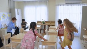 Back to school of adorable student entering classroom at elementary school. Caucasian teacher welcome and greeting group of young schoolboy and girl wearing backpack sit on table at kindergarten. - Powered by Shutterstock - Get 15% off with code: PIKWIZARD15