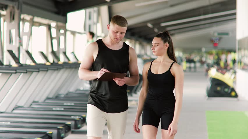 With a focus on individualized attention, a personal trainer takes the time to explain workout techniques to a woman, ensuring she comprehends and performs the exercises correctly.
