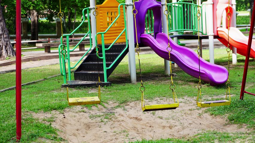 A colorful playground slide and swing on sandy park grounds for children.