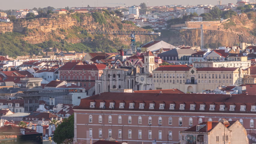 Baixa district with Santa Justa Lift timelapse and Convento da Ordem do Carmo historical church. Almada on a background. Aerial view from viewpoint do Monte Agudo during sunset. Lisbon, Portugal