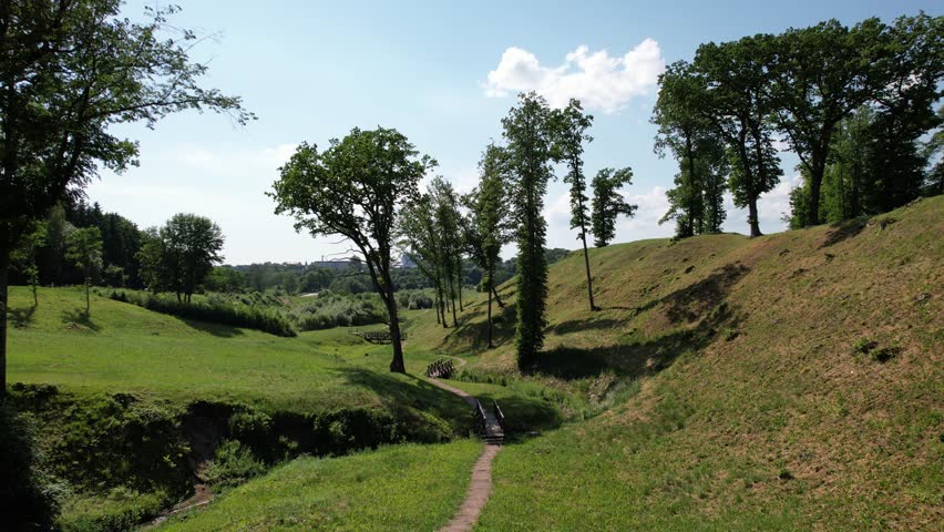 A captivating drone shot reveals a picturesque hill adorned with a winding walking path and charming bridges. The path meanders up the hillside, offering panoramic views of the surrounding landscape. 