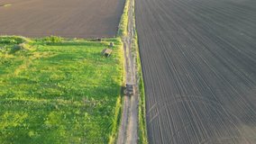 An aerial view of a truck driving on a dirt road through farm fields at sunset. The truck is driving between two fields, one with green grass and the other with dark soil. - Powered by Shutterstock - Get 15% off with code: PIKWIZARD15