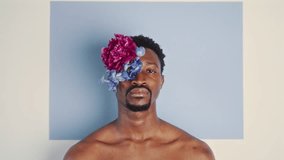 Young shirtless African American man wearing flower eyepatch posing on camera against pastel color background in studio. Video portrait - Powered by Shutterstock - Get 15% off with code: PIKWIZARD15