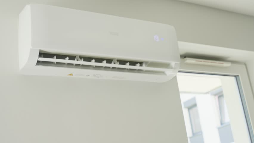 Adjusting air conditioner temperature with remote control. Hand holds remote control and setting comfortable temperature on climate system in apartment