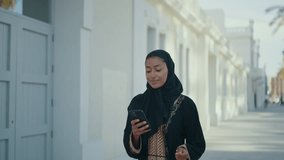 Cinematic image of a beautiful woman from Dubai wearing black abaya dress and walking in the city center and using the smart phone. - Powered by Shutterstock - Get 15% off with code: PIKWIZARD15